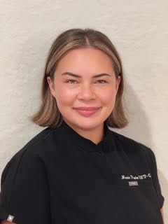 Young woman in chef's attire smiling at camera.